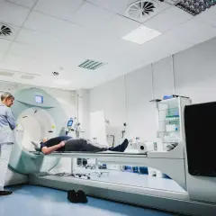 Pacjent leży na stole aparatu do scyntygrafii, podczas gdy technik przygotowuje badanie.