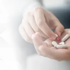 Dłoń trzymająca kapsułki, w tym jedną czerwoną i białą, przypominającą azytromycynę.