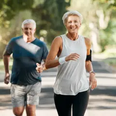 Szczęśliwa para seniorów biegnie po leśnej ścieżce, ciesząc się aktywnym stylem życia i piękną pogodą.