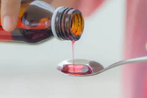 Czerwony syrop na kaszel mokry kapie z butelki na łyżeczkę.