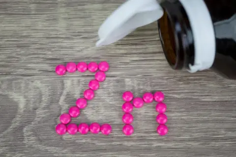 Różowe tabletki ułożone w napis "Zn" na drewnianym tle. Suplement cynku na co? Na odporność, skórę i włosy.