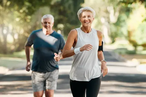 Szczęśliwa para seniorów biegnie po leśnej ścieżce, ciesząc się aktywnym stylem życia i piękną pogodą.