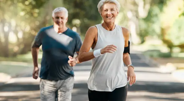Szczęśliwa para seniorów biegnie po leśnej ścieżce, ciesząc się aktywnym stylem życia i piękną pogodą.