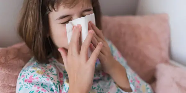 Dziewczynka z katarem wyciera nos chusteczką. Może potrzebuje antybiotyku na zatoki.